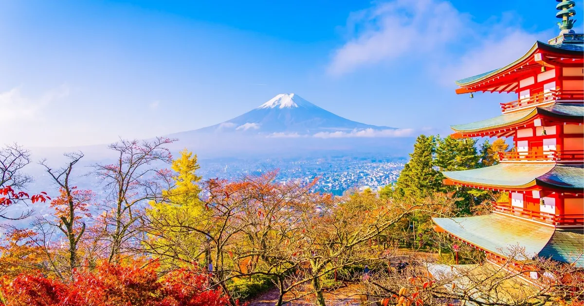 The red Chureito Pagoda among orange and yellow autumn trees, with snow-capped Mount Fuji behind under a blue sky
