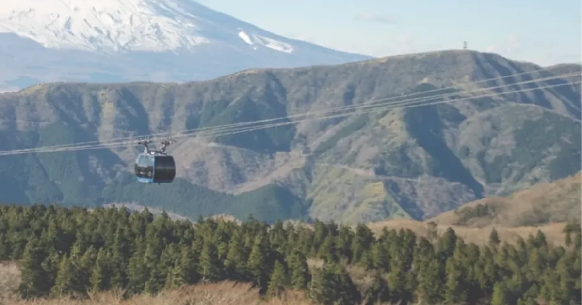 A Hakone Ropeway gondola crossing the wooded ridges above Owakudani with Mount Fuji behind