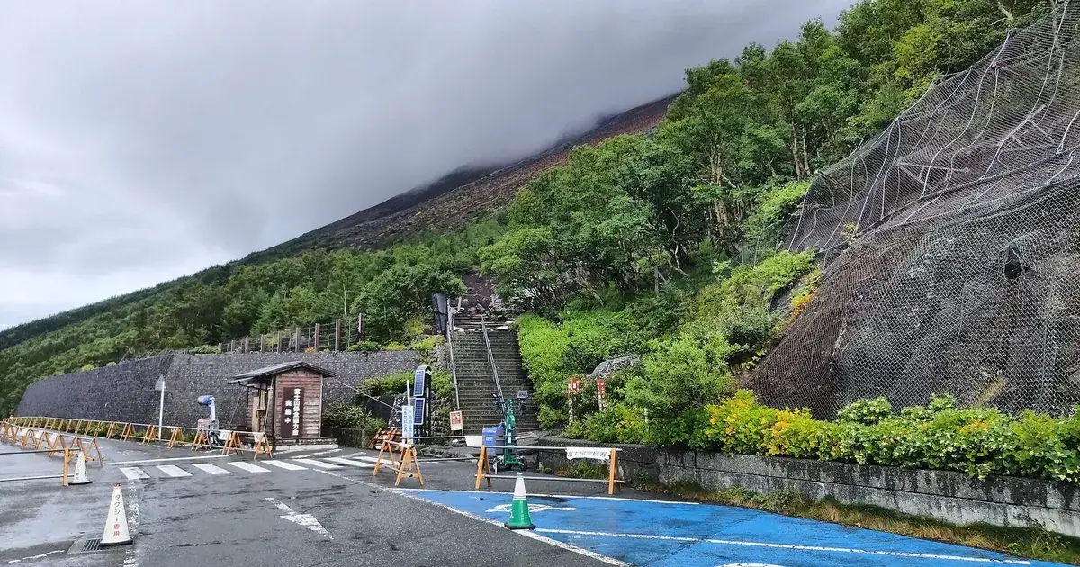 The start of the Fujinomiya Trail at Mount Fuji's Fujinomiya 5th Station: stone steps climbing from the car park into green scrub, with the mountain's reddish upper slopes disappearing into low cloud